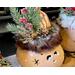 This shows the greenery decorating the elf hat. It is nestled together with, jingle bells, pinecones, and the faux fur trim around the hat.